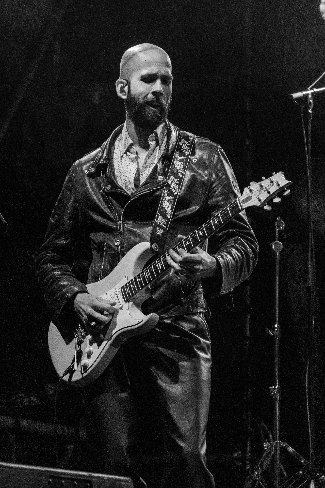 Gitarist met baard en zwart vest op podium met microfoon
