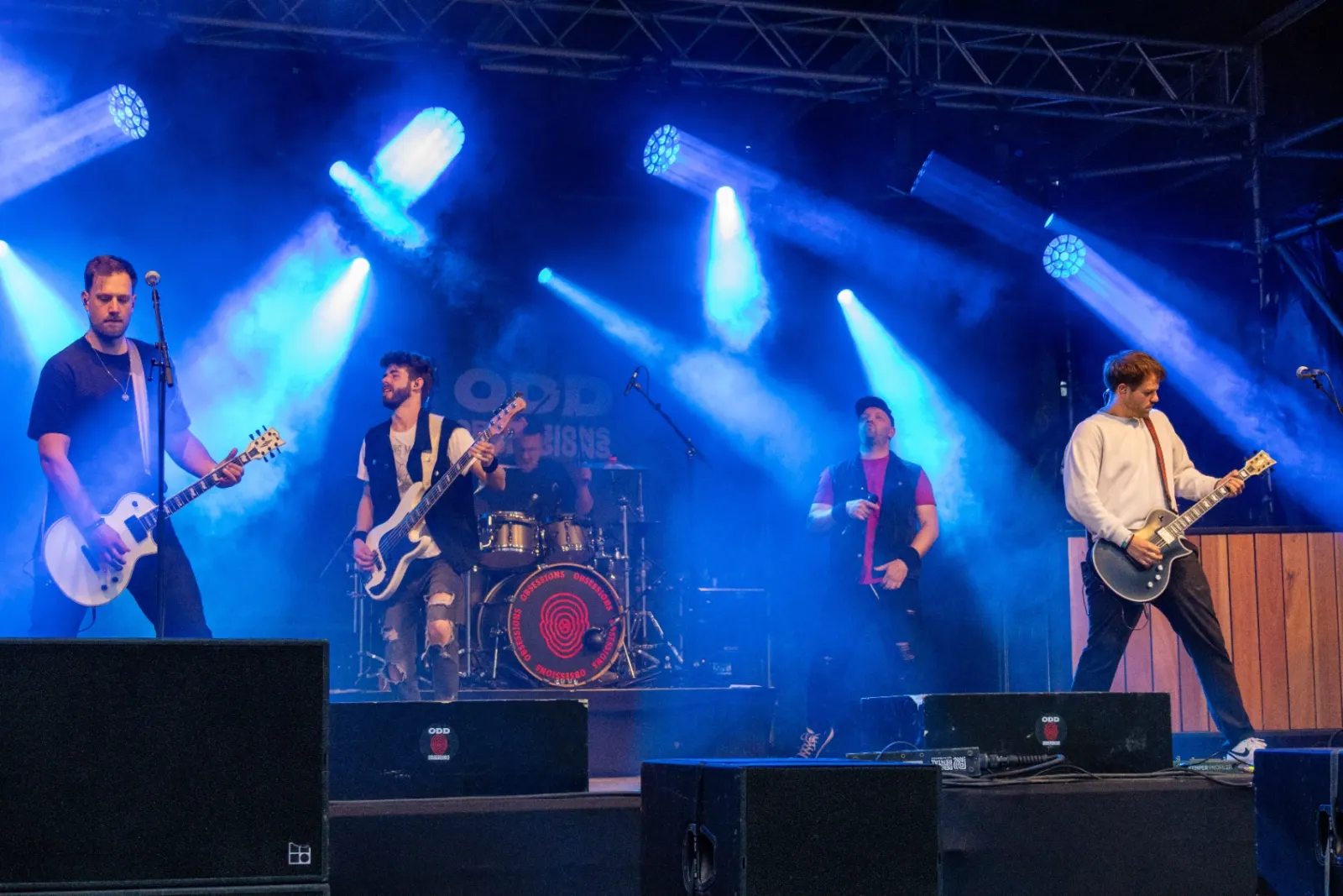Vijfkoppige band op festivalpodium met blauwe lichtshow en rook