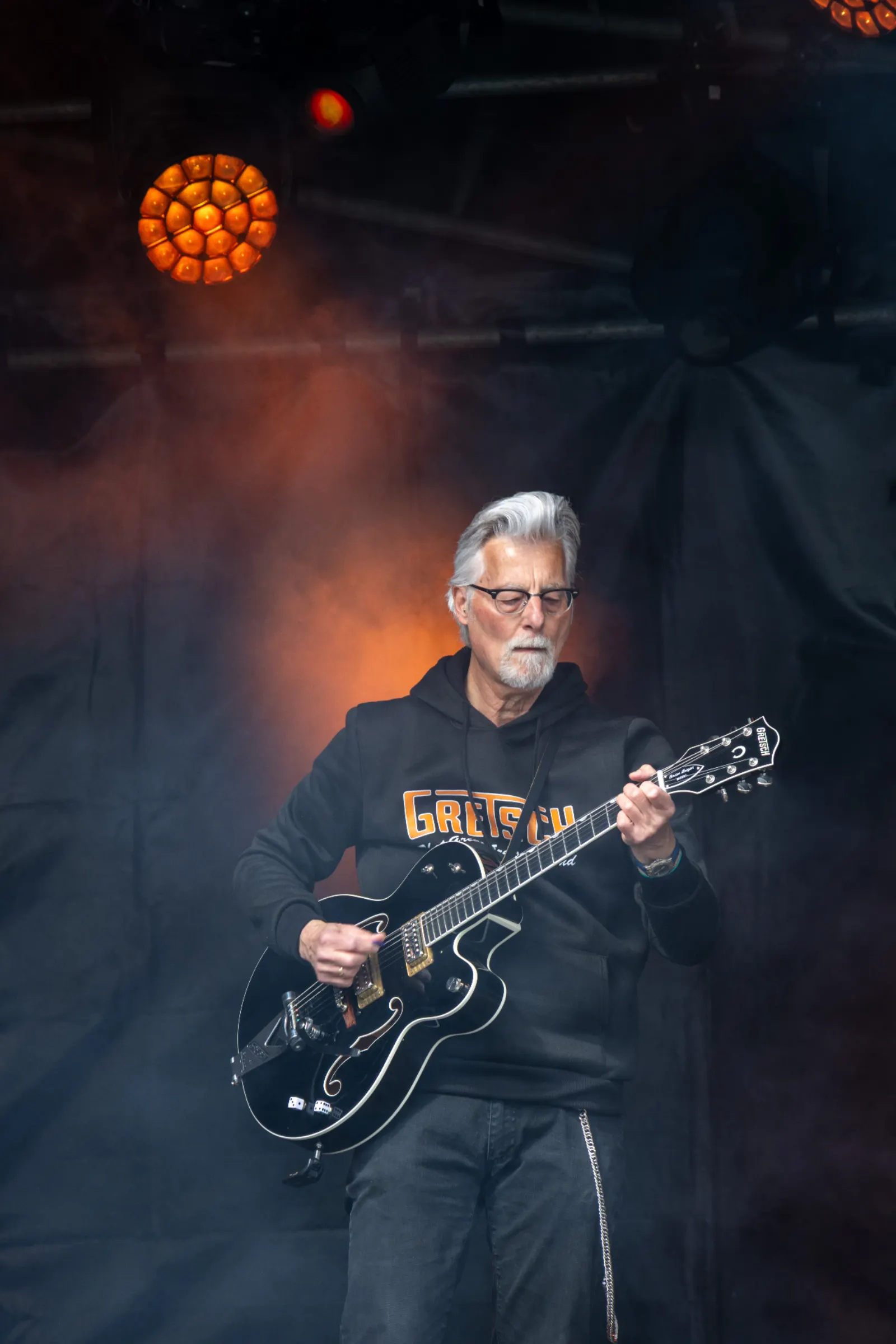Gitarist met Gretsch hollowbody op podium met oranje tegenlicht en rook