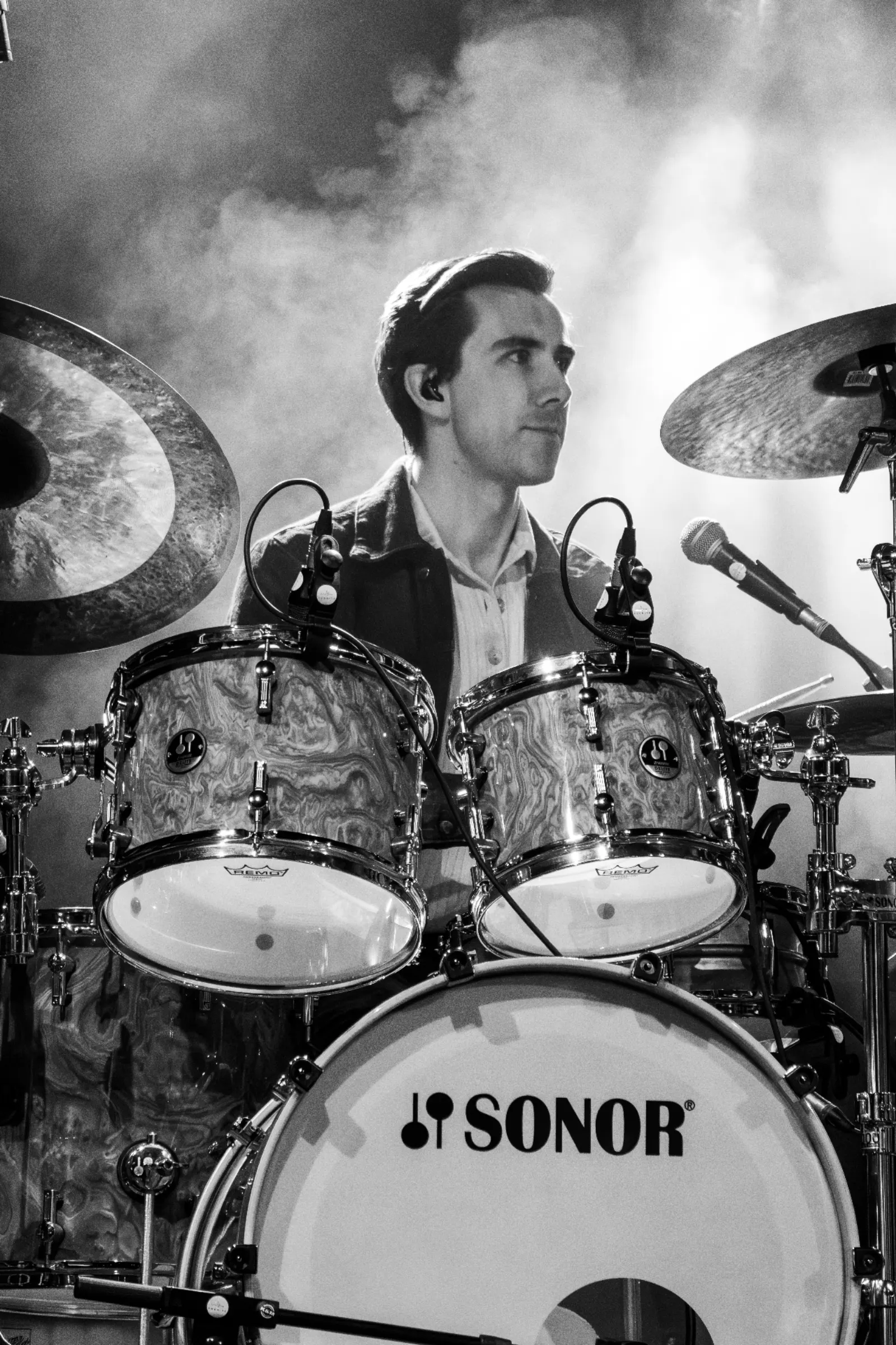 Zwart-wit portret van drummer met in-ears achter Sonor drumkit met rook op de achtergrond