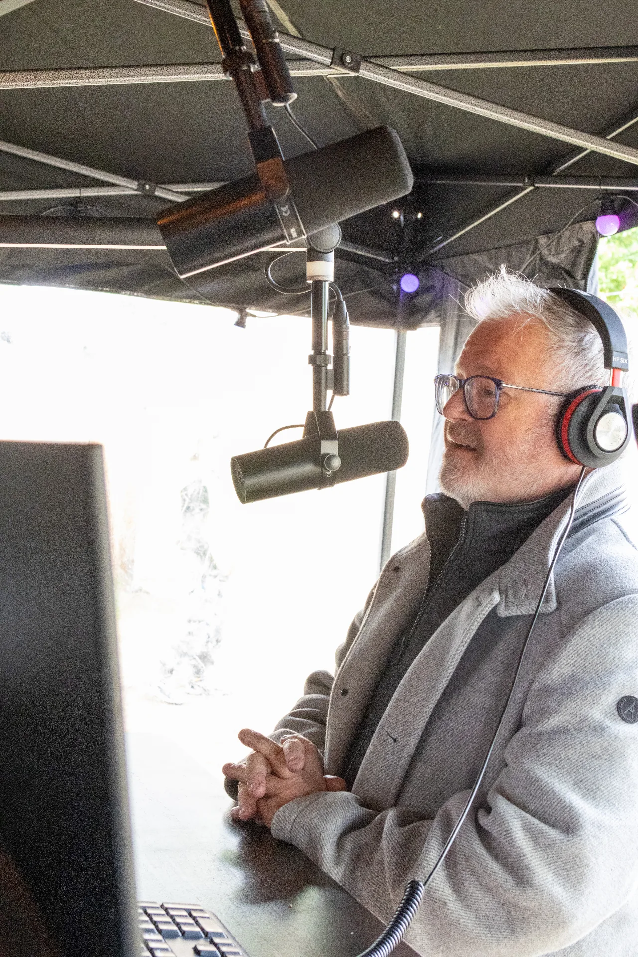 Presentator met koptelefoon achter broadcast microfoon in mobiele studio