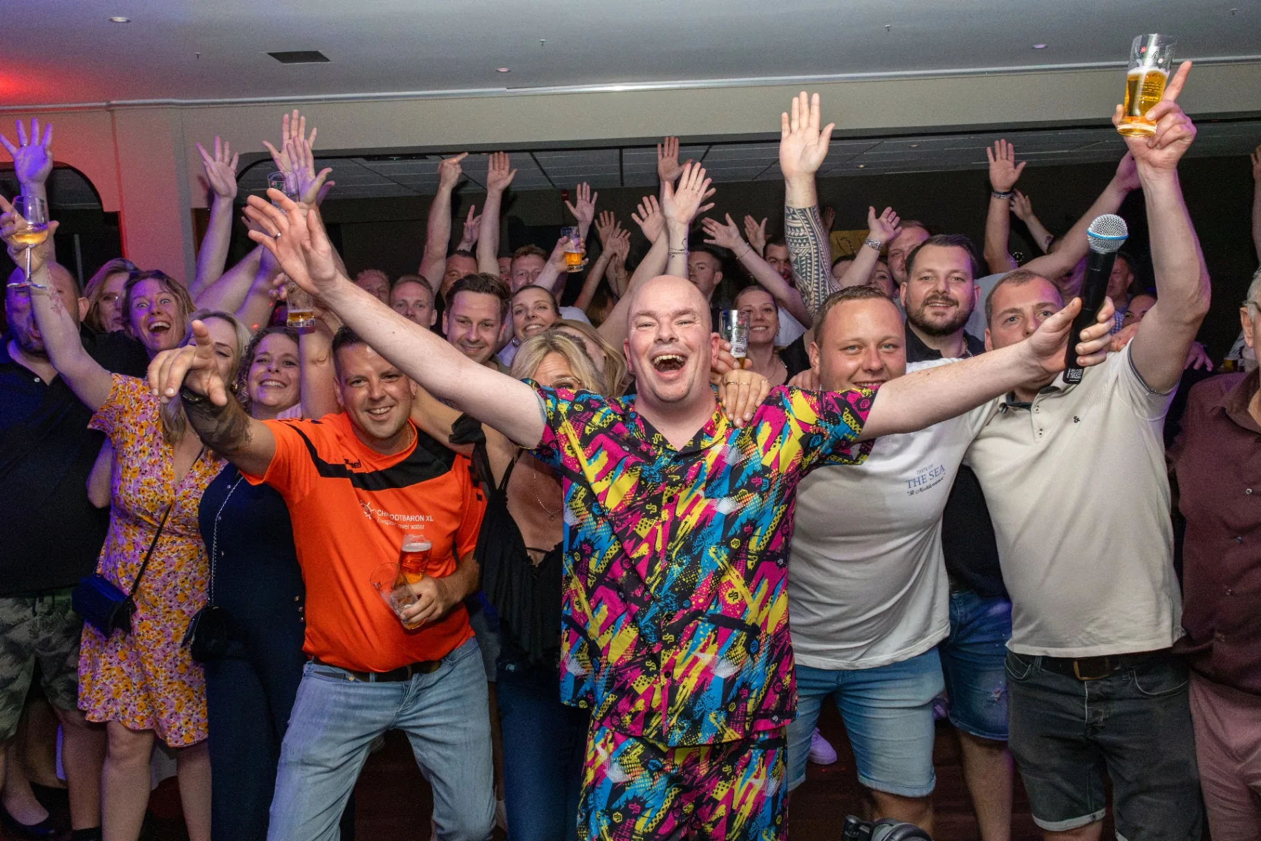 Juichend publiek met opgestoken armen op feest met kleurrijk shirt in het midden