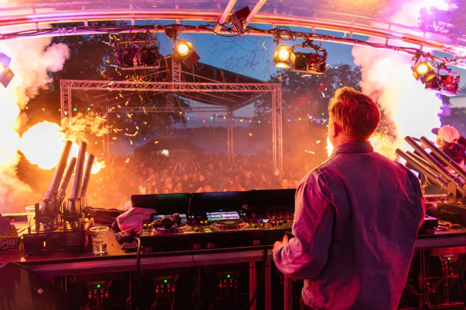 Feest DJ Ruud podium met grote vlinderdecors, paddenstoelen, vuurwerk fonteinen en juichend publiek bij schemering