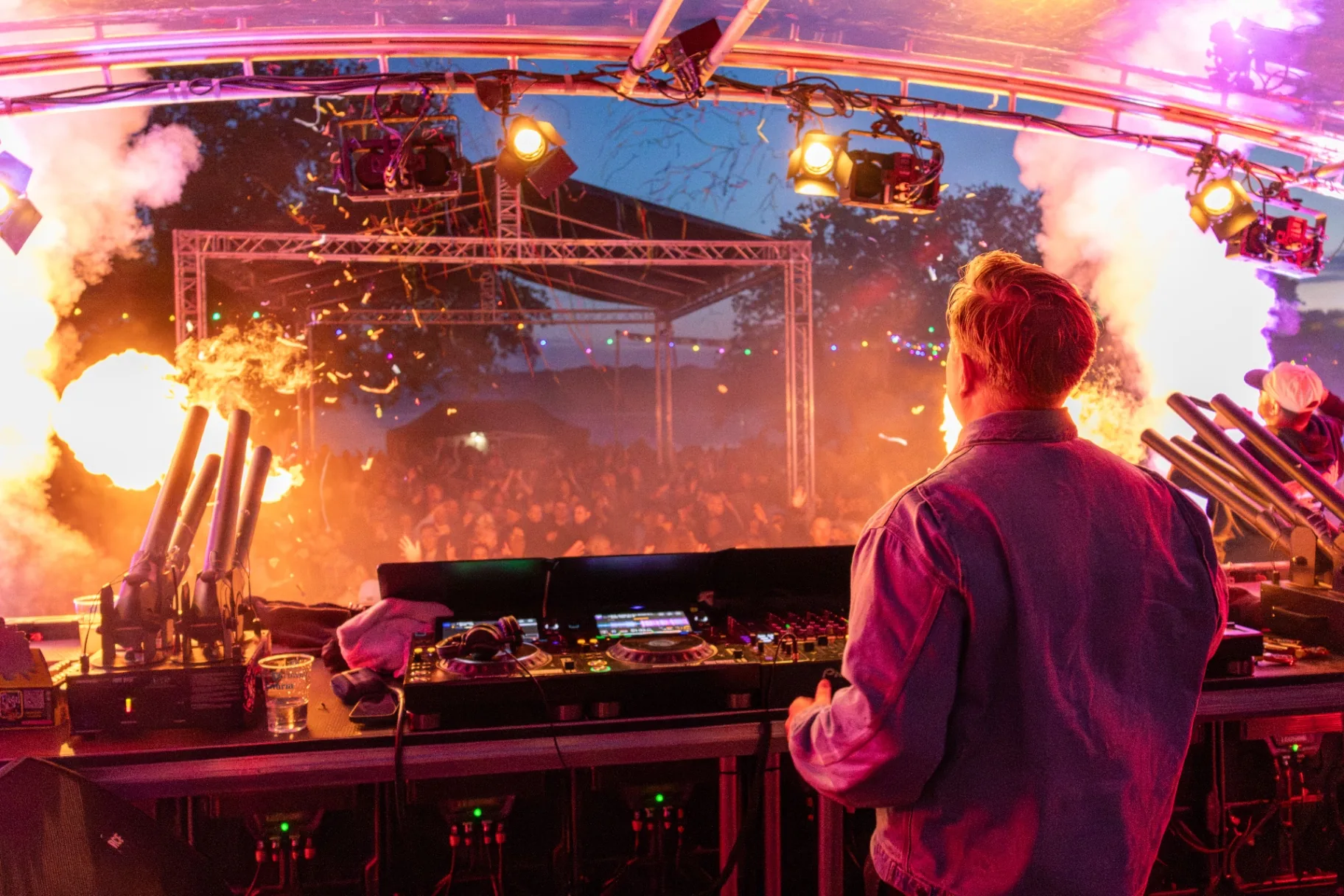 DJ tussen vuurwerk fonteinen met oranje rook op festivalpodium
