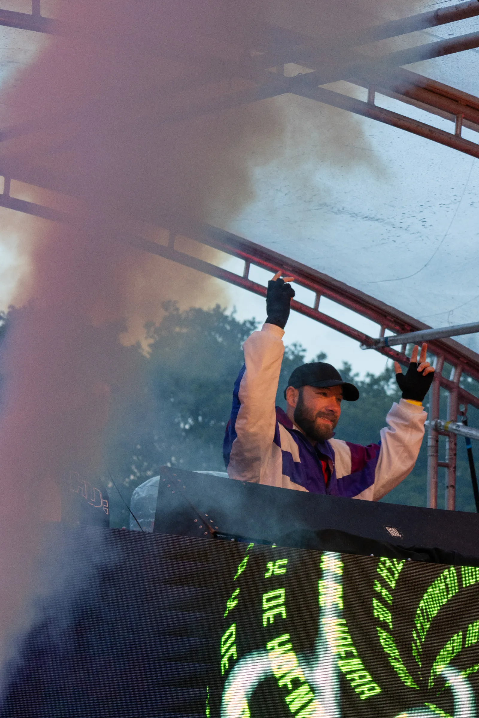 DJ met handen omhoog achter draaitafel met rook en groene LED visuals