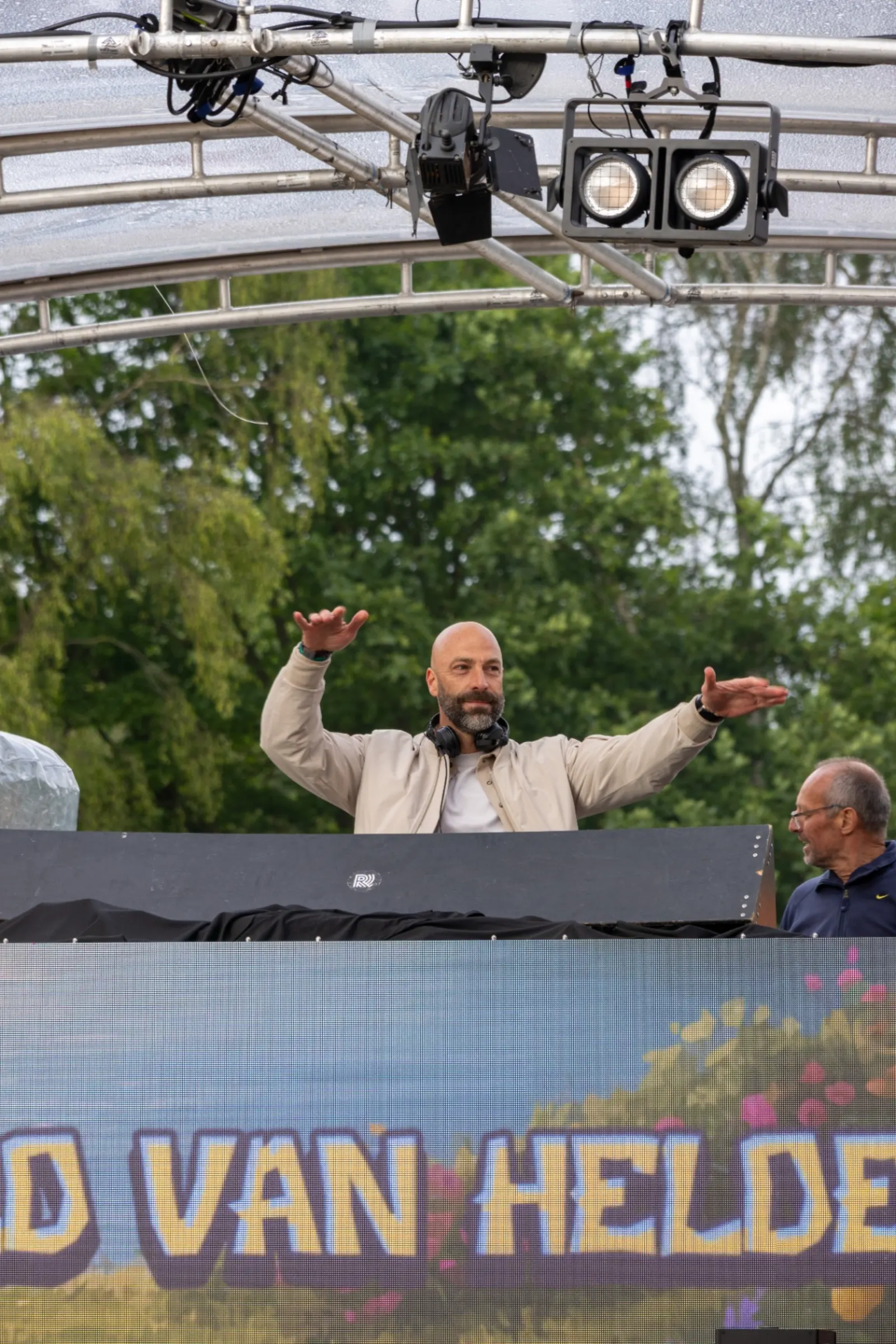 DJ met handen wijd op outdoor festivalpodium met LED scherm