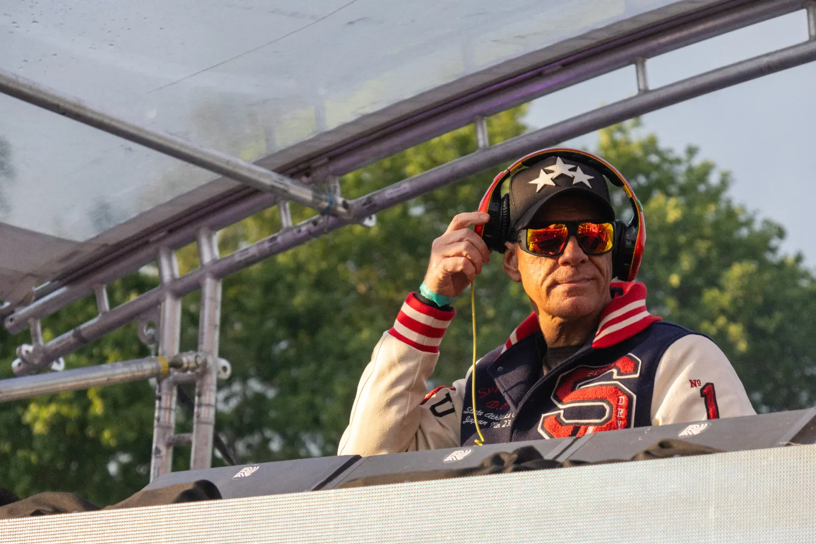 DJ met zonnebril en baseballjack achter draaitafel in gouden avondlicht