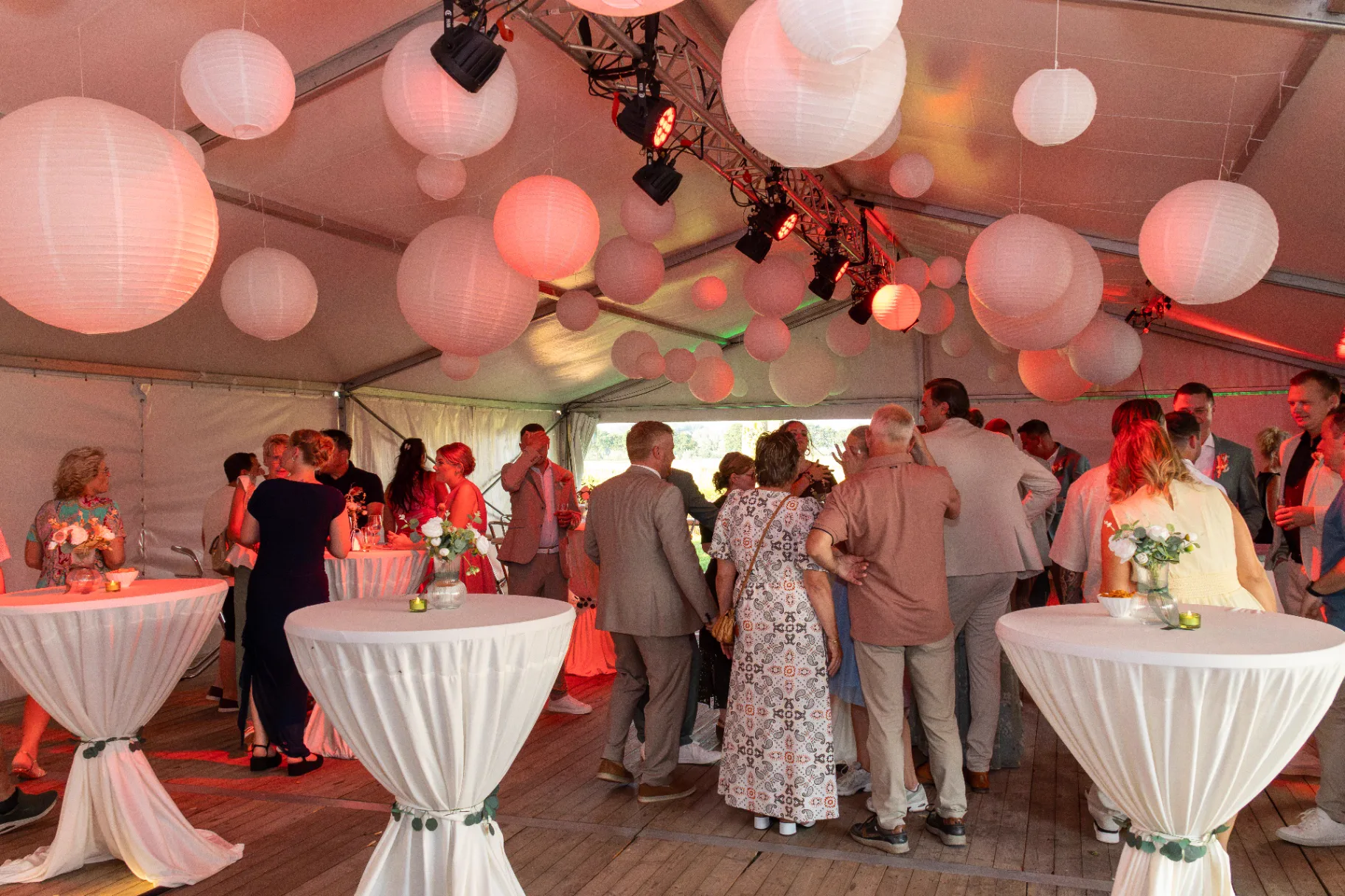 Bruiloftsgasten onder witte lampionnen in feesttent bij zonsondergang
